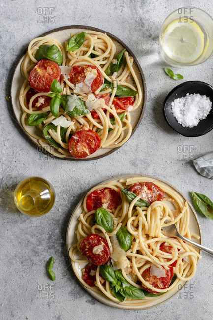 Two plates of bucatini pasta with roasted tomatoes and basil
