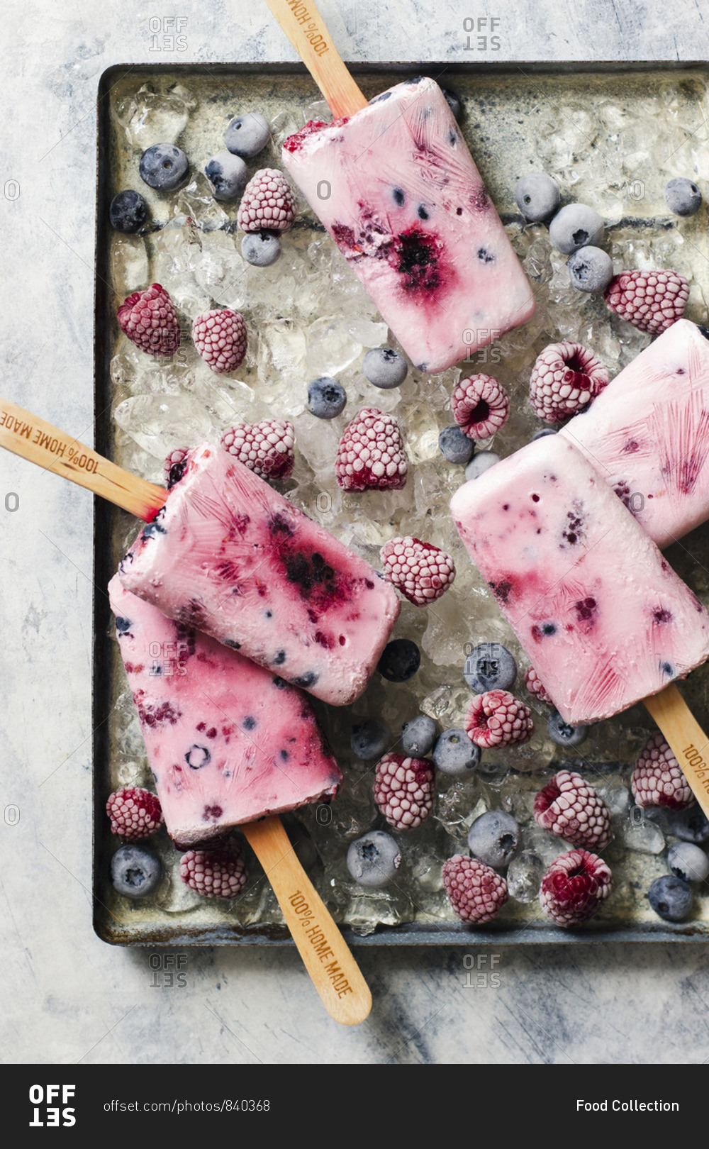 Homemade ice cream popsticles from yogurt, honey and berries, raspberries and blueberries on ice