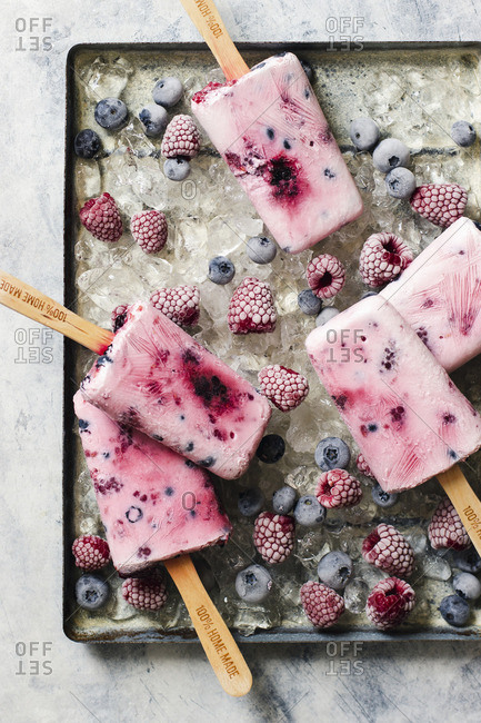 Homemade ice cream popsticles from yogurt, honey and berries, raspberries and blueberries on ice
