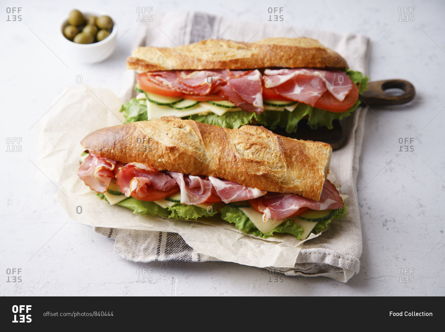 Side view of two fresh baguette sandwiches bahn-mi styled with ham, sliced cheese, tomatoes and fresh lettuce