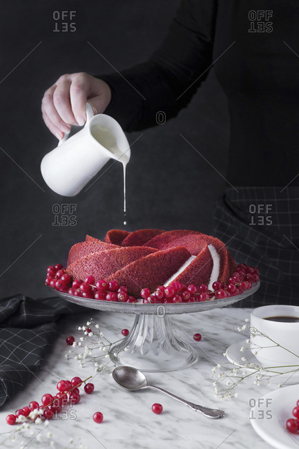 Woman serving and pouring cream on sweet red cake
