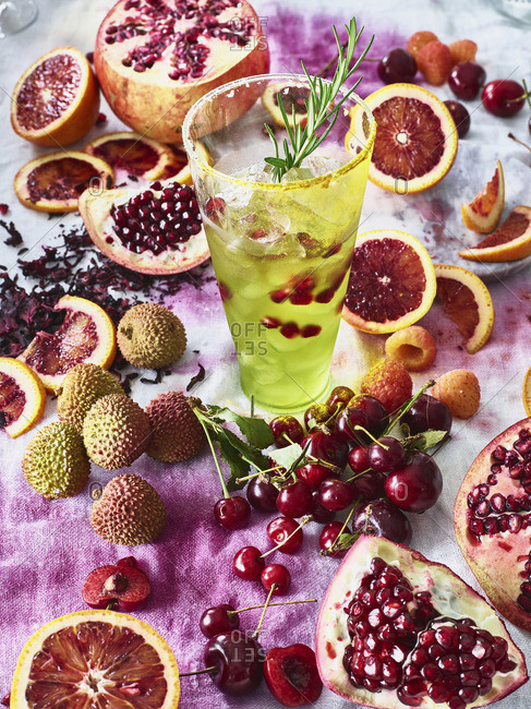 A green cocktail in a glass with pomegranate and rosemary