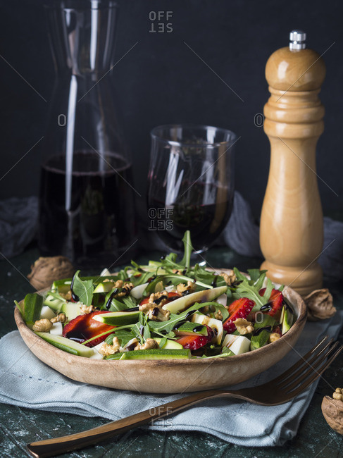 Raw salad with strawberries, zucchini, arugula, walnuts and cheese drizzled with balsamic glaze