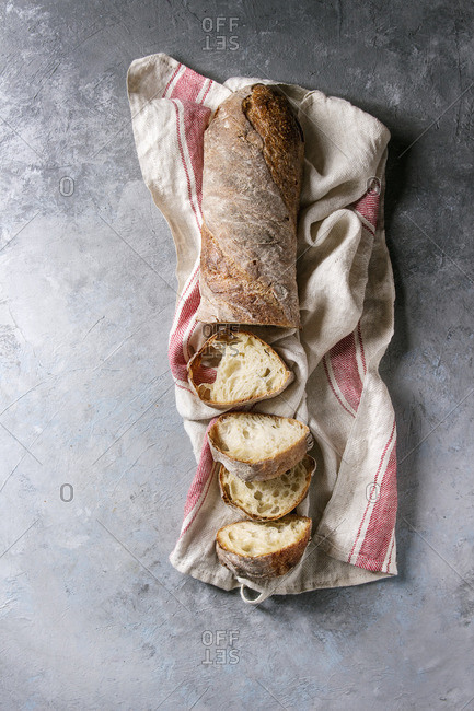 Sliced fresh baked artisan whole grain ciabatta bread on kitchen towel over grey texture background