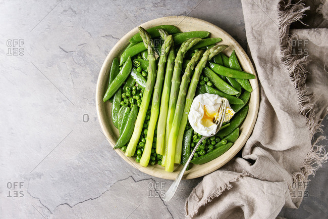 Variety of cooked green vegetables asparagus, peas, pod pea, served with bread and poached egg