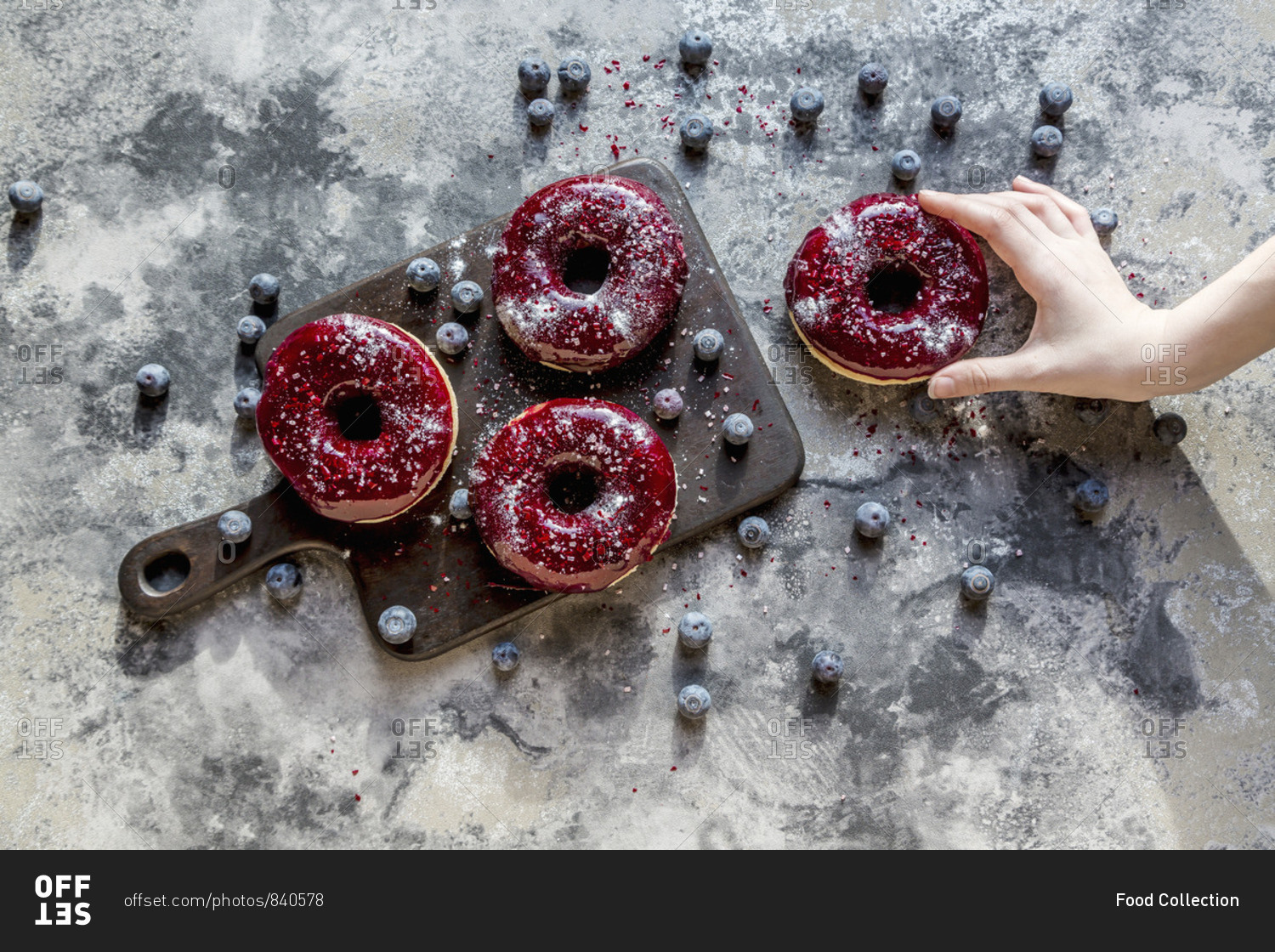 A hand taking a doughnut with blueberry glaze and glitter powder