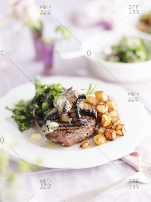 A beef steak with mushrooms, garlic butter, salad, vegetables and potatoes
