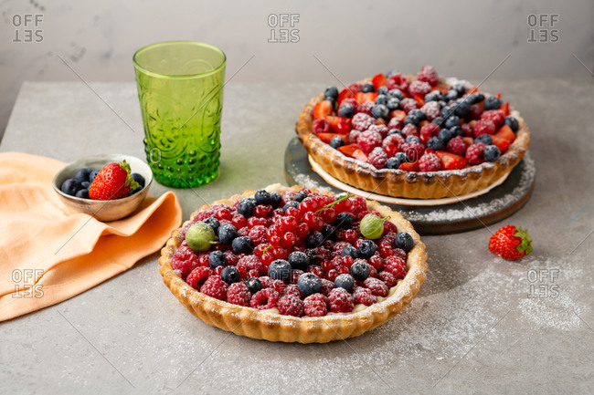 Two freshly made berry tarts sprinkled with powdered sugar
