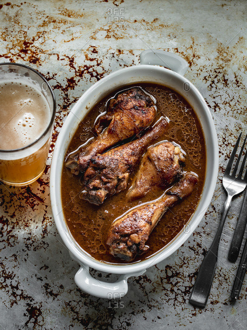 Marinated baked chicken drumstick in thai pepper sauce in baking dish with beer in tall glass on the side