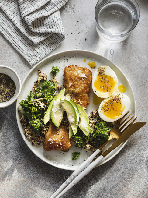 Baked fish with quinoa, kale and avocado with soft boiled eggs on the side served on white plate
