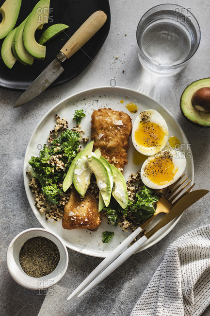 Baked fish with quinoa, kale and avocado with soft boiled eggs on the side served on white plate