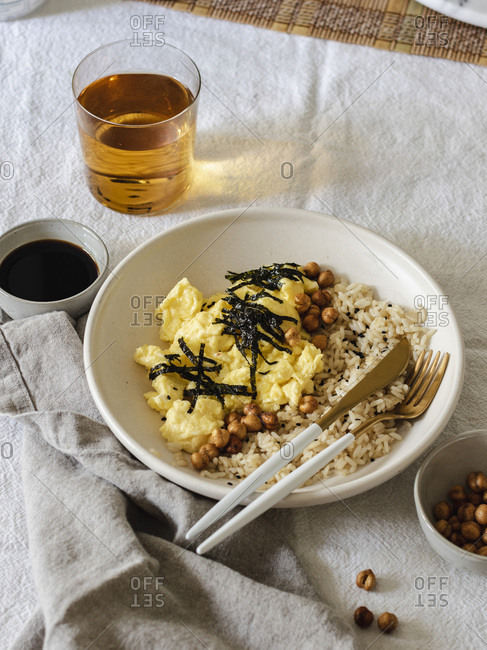 Japanese style scrambled eggs with rice chickpeas and nori served in white bowl with fork and knife
