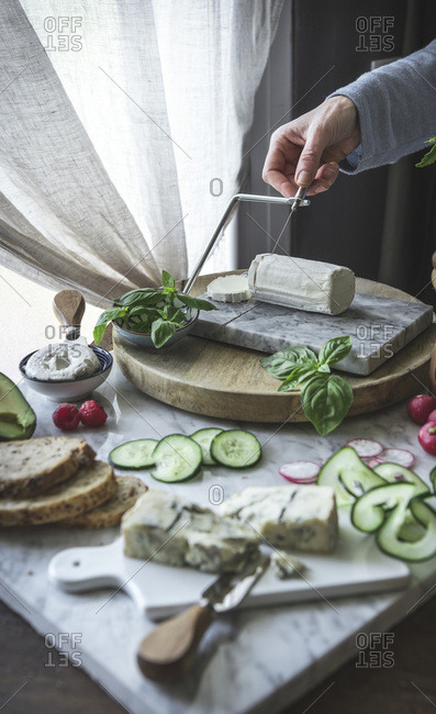 A woman slicing soft cheese on a cheese board, with various vegetables.