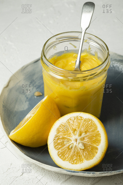 Fresh lemons,  sliced in half, arranged on a blue hand made plate, with a spoon in a jar of home made lemon curd.