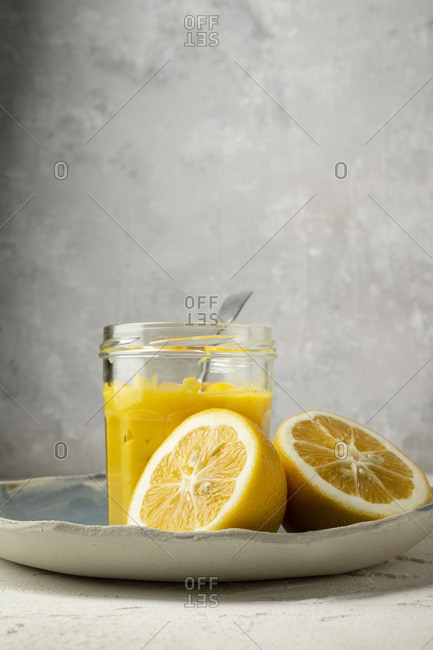 Fresh lemons,  sliced in half, arranged on a blue hand made plate, with a spoon in a jar of home made lemon curd.