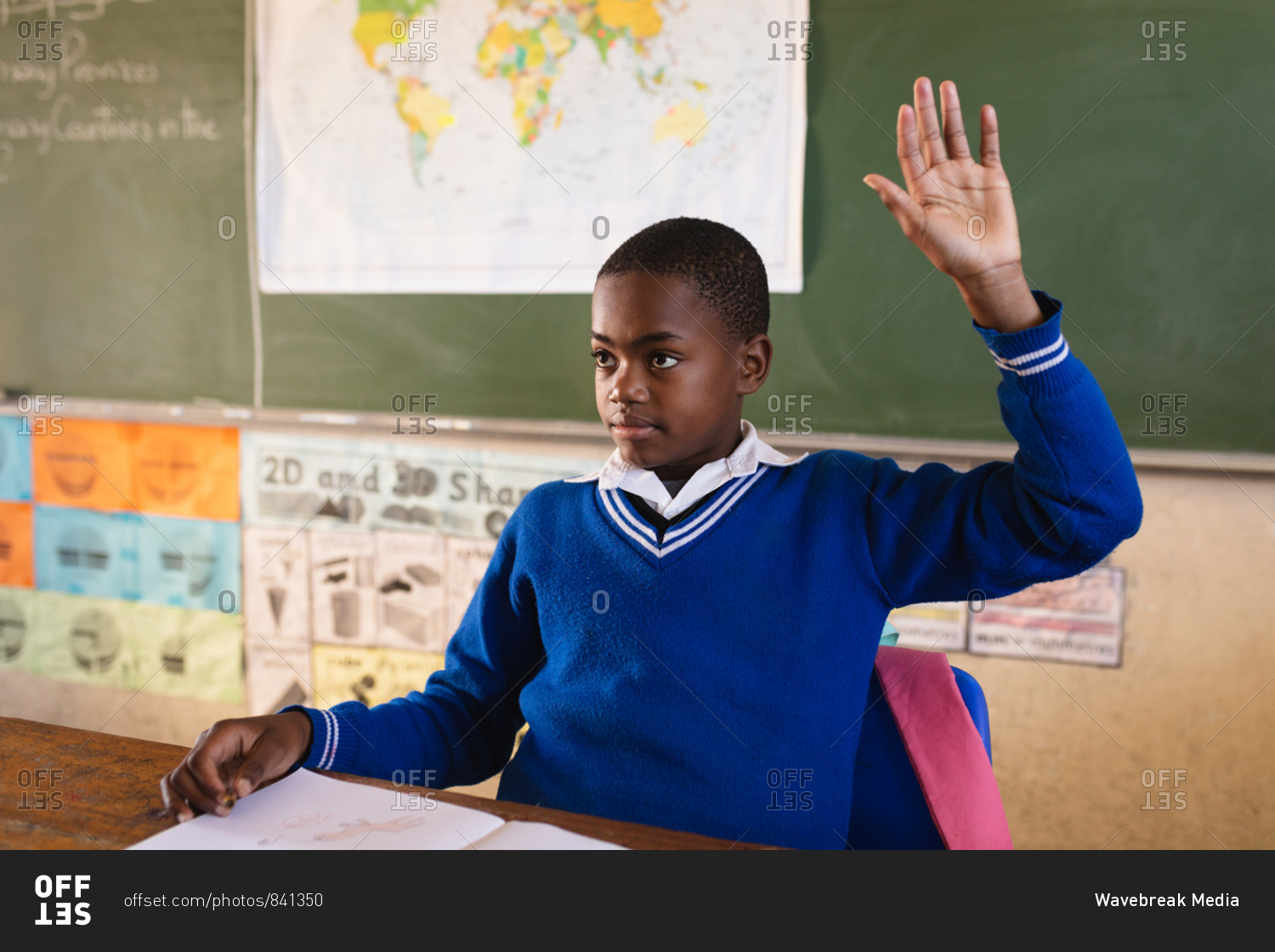 African schoolboy sitting at a desk and raising his hand to answer a