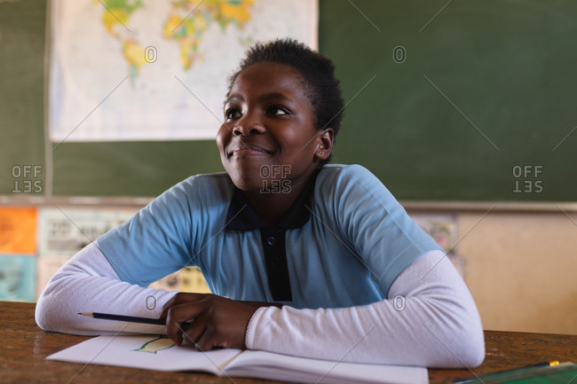 Front view close up of a young African schoolgirl sitting at a desk smiling and listening attentively during a lesson in a township elementary school classroom