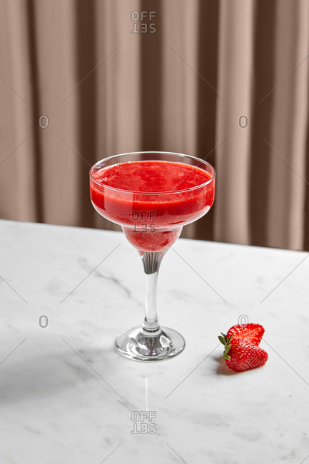 Tasty aromatic strawberry smoothie in glass bowl on high leg and sliced strawberry on marble table