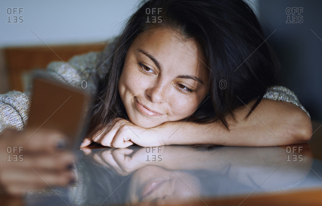 Woman at home sitting at the table and using smartphone