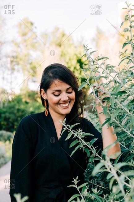 Beautiful brunette woman standing among blooming bushes in park and looking away in lisbon