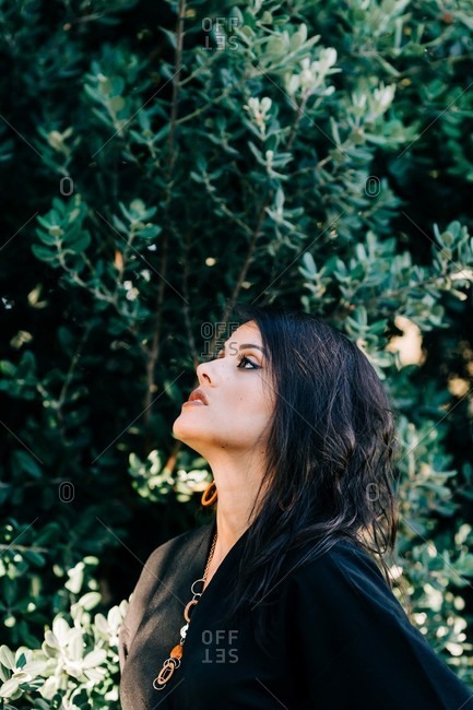 Beautiful brunette woman standing among blooming bushes in park and looking away in lisbon