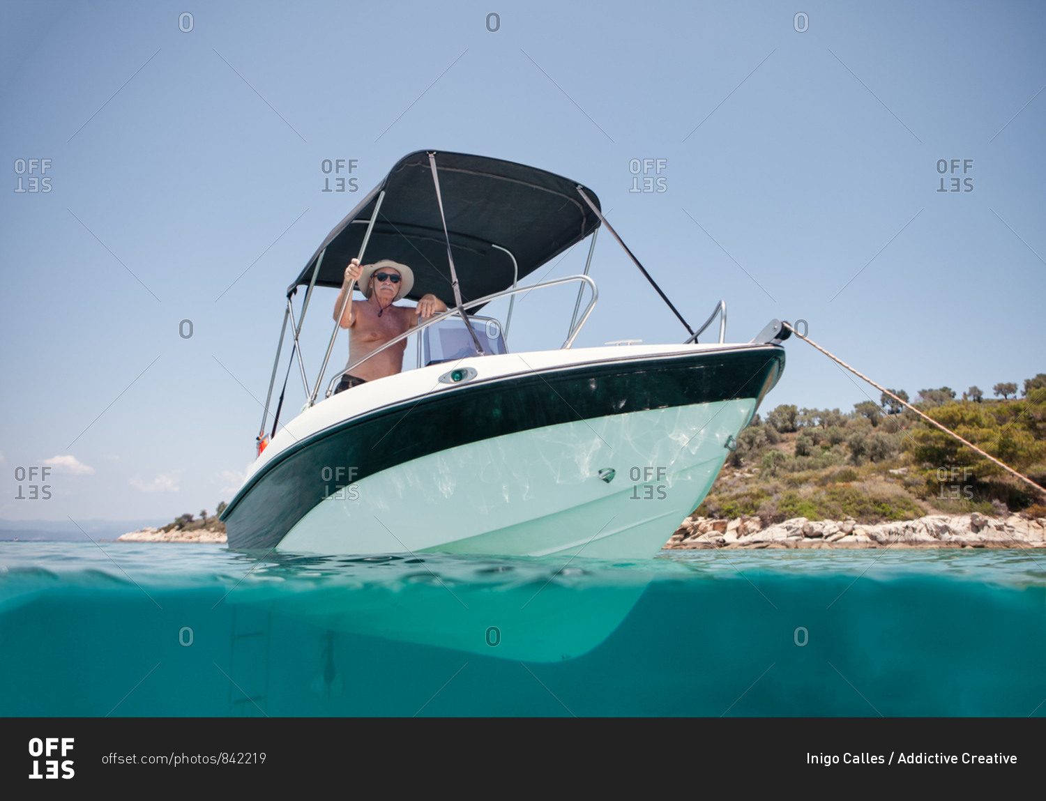 From below elderly man in hat and sunglasses sailing on black and white boat in calm turquoise water of halkidiki, greece