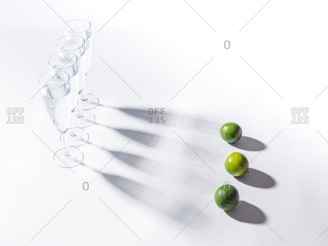 Contrasting shadows from glasses of water and green ripe limes on white background