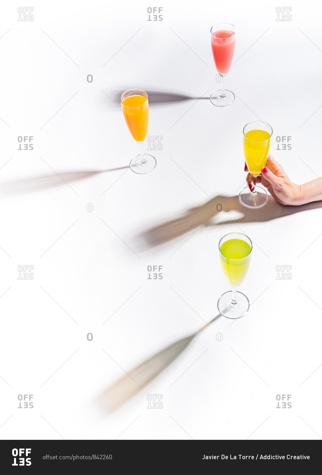 Woman crop hands holding a glass of juicy appetizing yellow near orange and red drinks on white background