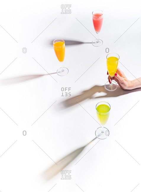 Woman crop hands holding a glass of juicy appetizing yellow near orange and red drinks on white background