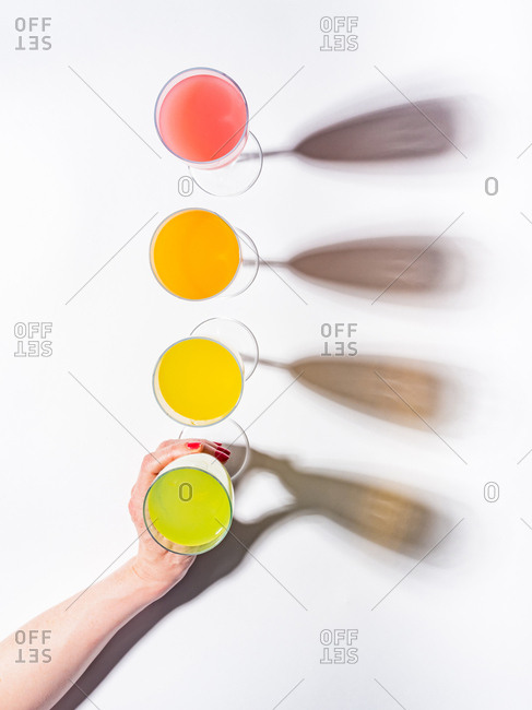 Woman crop hands holding a glass of juicy appetizing yellow near orange and red drinks on white background