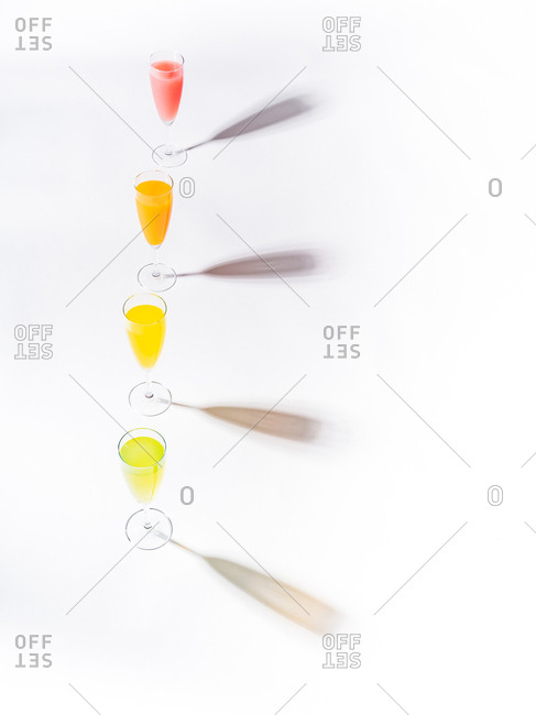 Contrasting shadows from glasses of juicy appetizing orange red yellow green drinks on white background