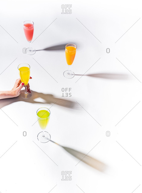 Woman crop hands holding a glass of juicy appetizing yellow near orange and red drinks on white background