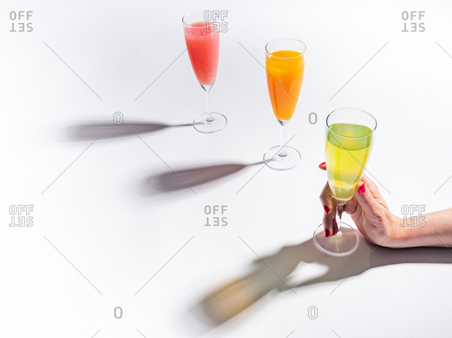 Woman crop hands holding a glass of juicy appetizing yellow near orange and red drinks on white background