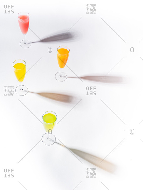 Contrasting shadows from glasses of juicy appetizing orange red yellow green drinks on white background