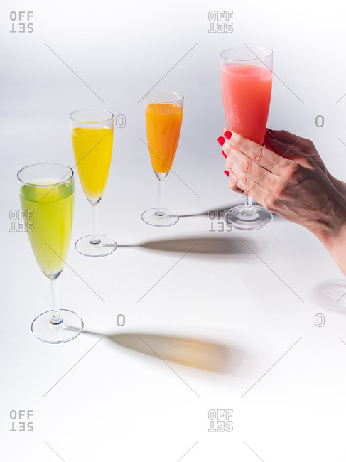 Woman crop hands holding a glass of juicy appetizing yellow near orange and red drinks on white background