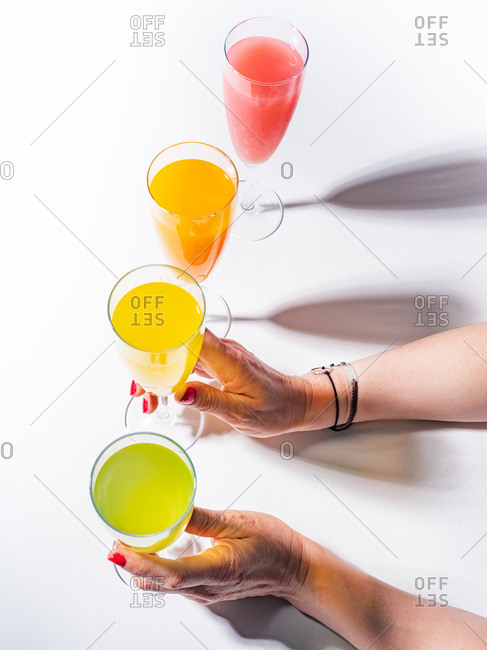 Woman crop hands holding a glass of juicy appetizing yellow near orange and red drinks on white background