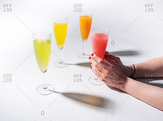 Woman crop hands holding a glass of juicy appetizing yellow near orange and red drinks on white background
