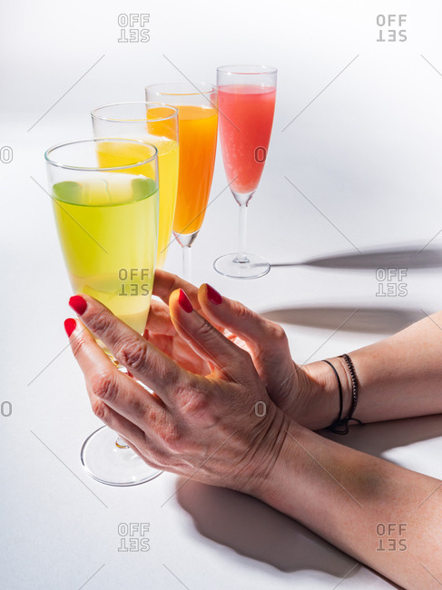 Woman crop hands holding a glass of juicy appetizing yellow near orange and red drinks on white background