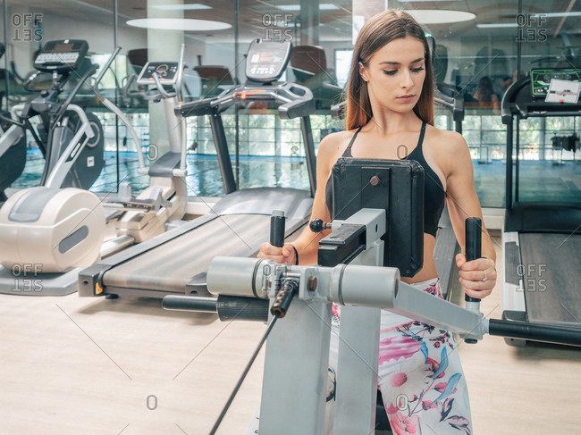 Focused fit woman in sportswear looking away while exercising on seated row machine in gym