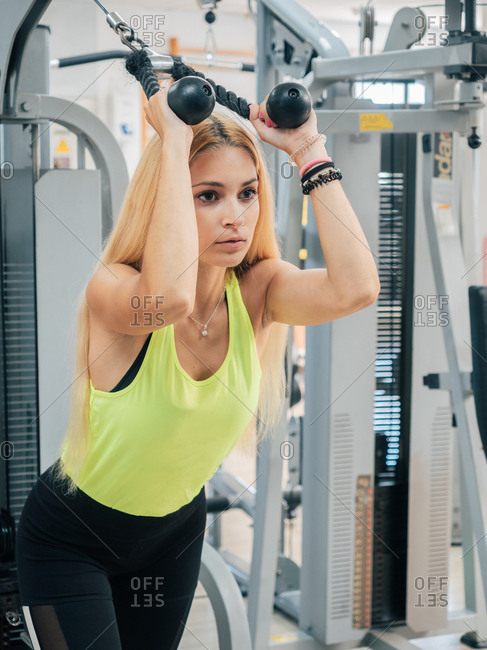 Strong young lady in sportswear pulling rope of exercise machine while training triceps and working out in modern gym
