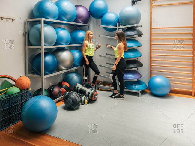 Side view of young ladies in sportswear standing near stands with equipment during break in workout in gym