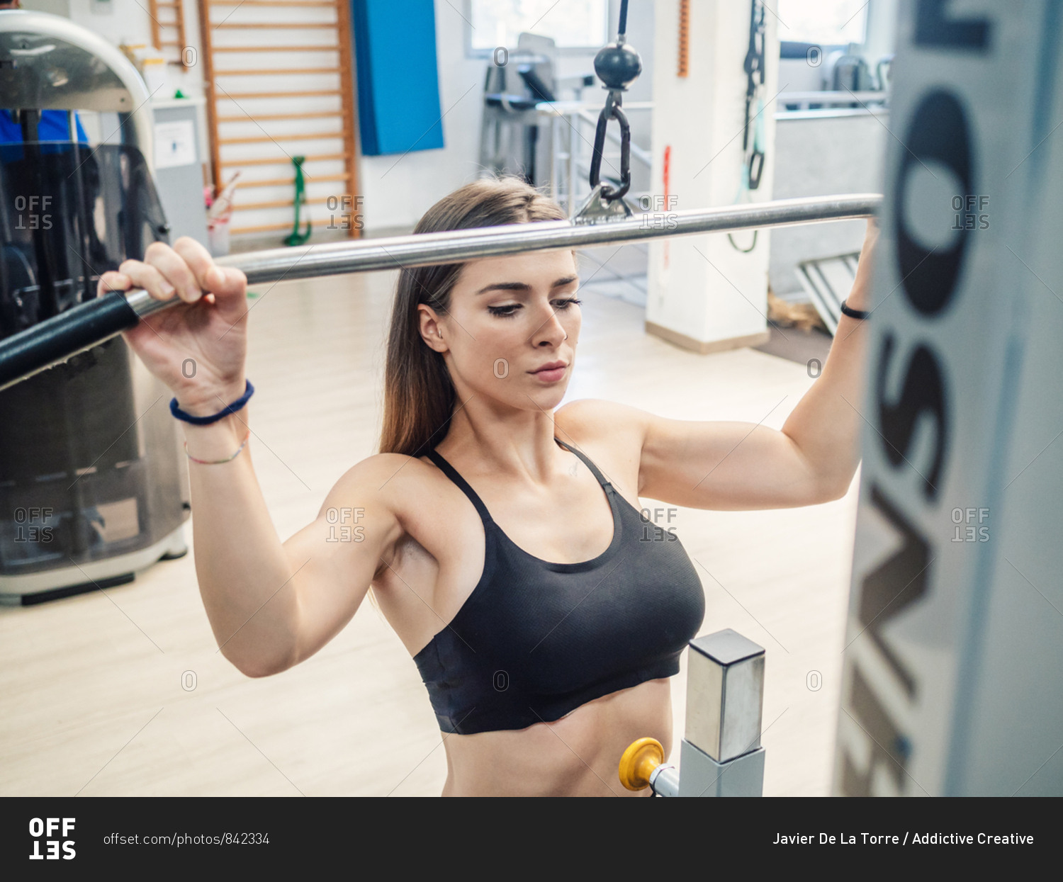 Slim sportswoman pulling down bar of exercise machine during training ...