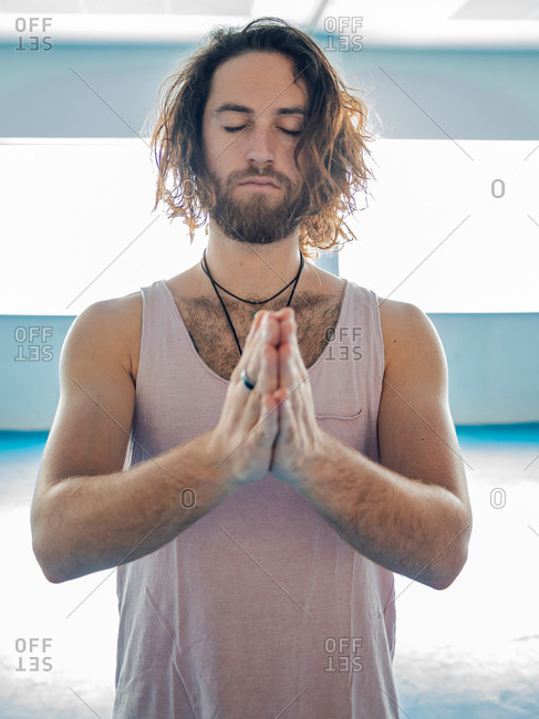 Bearded man in sportswear standing in one leg with prayer hands looking away on blue floor in studio
