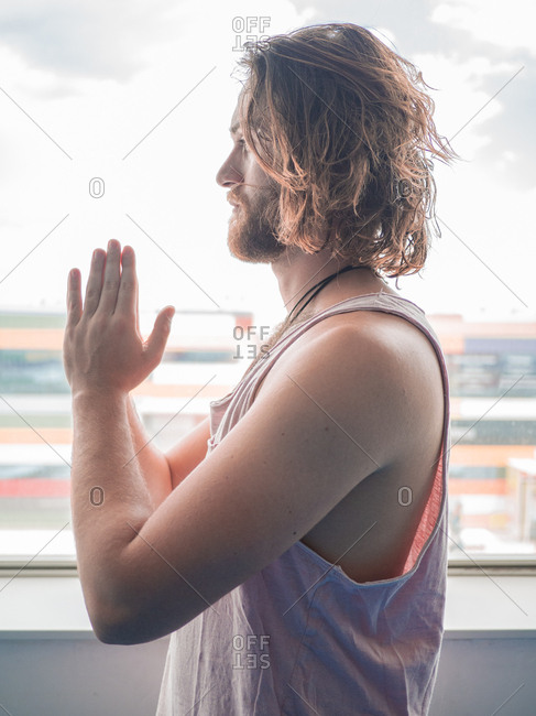 Bearded man in sportswear standing in one leg with prayer hands looking away on blue floor in studio
