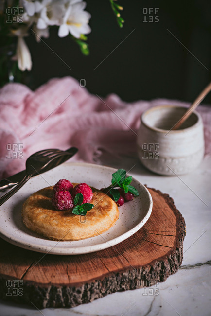 Tasty golden brown pancake topped with fresh raspberry and mint leaves on stylish white plate on marble tabletop
