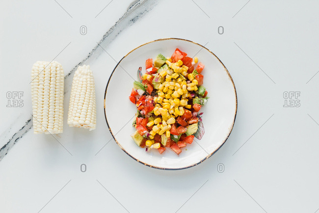 Served bowl with corn and cut tomatoes and zucchinis on table with tomatoes and corn
