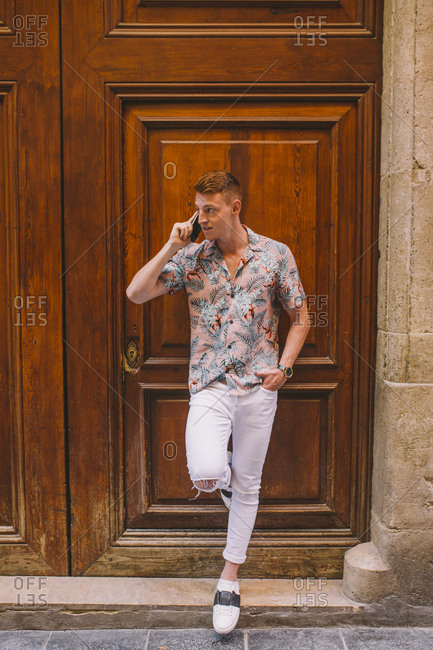 Handsome man talking on smartphone and leaning on wooden door looking away with hand in pocket