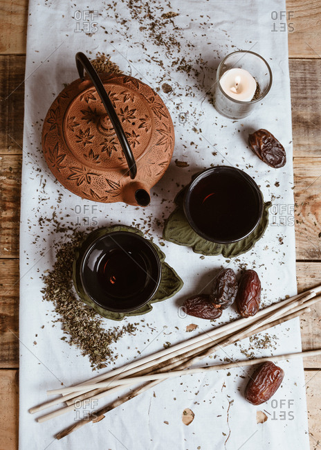 From above fragrant tasty tea in cup clay teapot and sweet dates on white tray decorated with tea leaves on wooden background