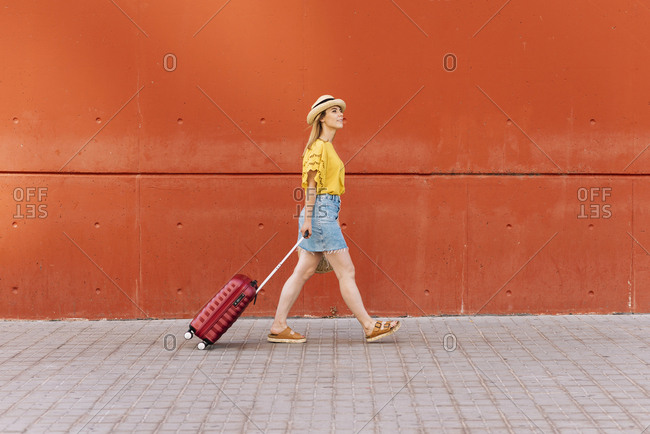 Side view of young beautiful female tourist going on adventure with suitcase