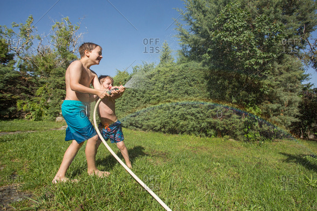 Little children in swimwear splashing water holding garden hose together